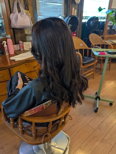 Long, dark brunette hair styled in loose waves, seen from behind in a salon chair