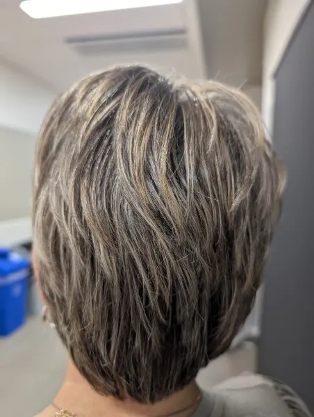 Short, stacked, textured cut with blonde highlights through brunette hair, seen from behind